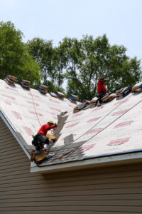 Crosby Roofing crew member installing a new roof, with shingle bundles staged for installation